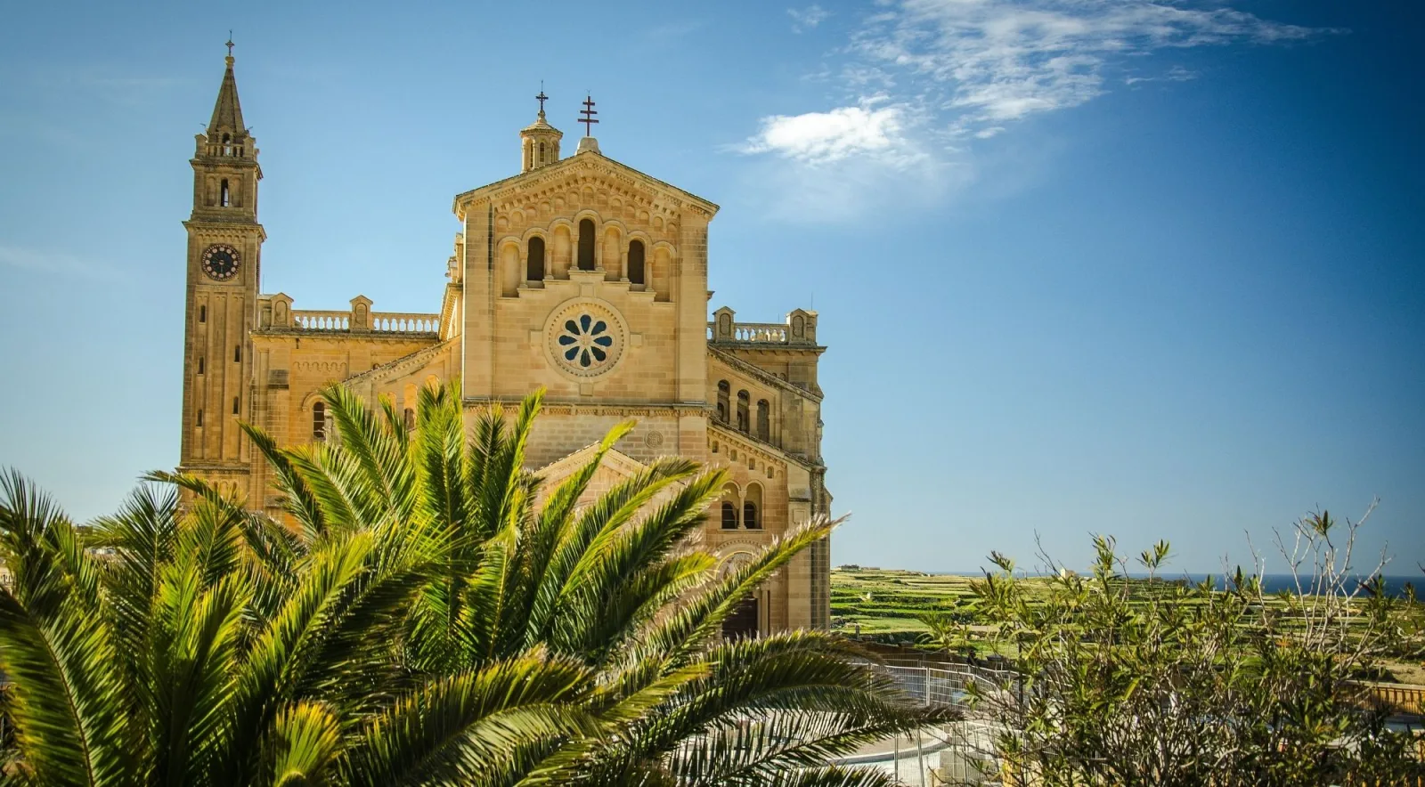 The twin-towered Ta' Pinu Basilica on Gozo seen past palm fronds under a blue sky