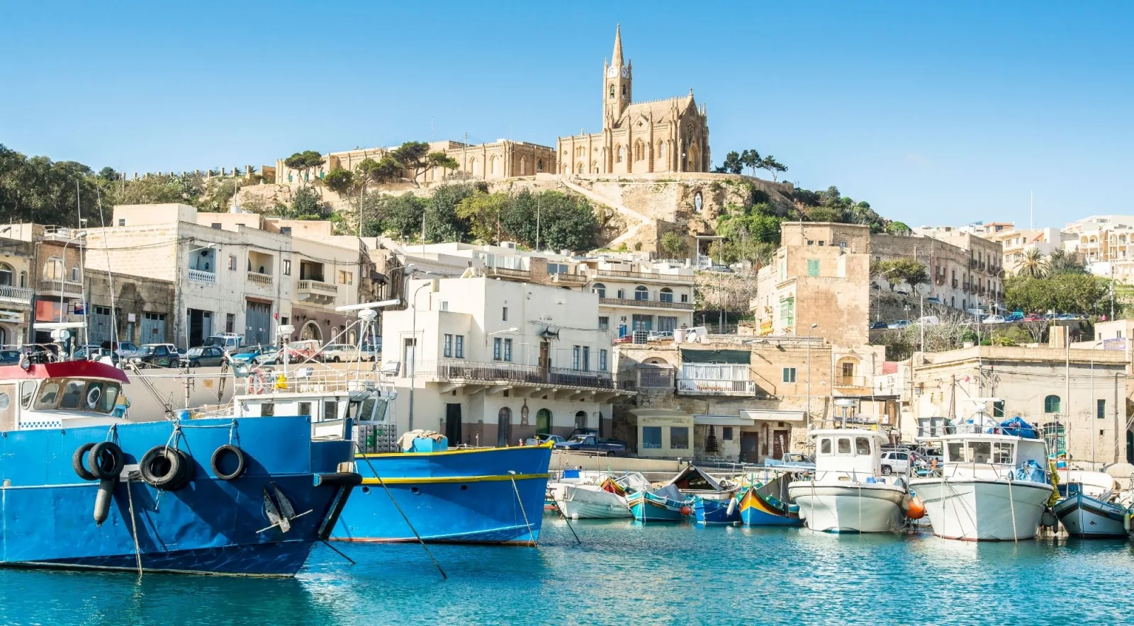 Fishing boats moored at Mġarr Harbour on Gozo below the church of Our Lady of Lourdes