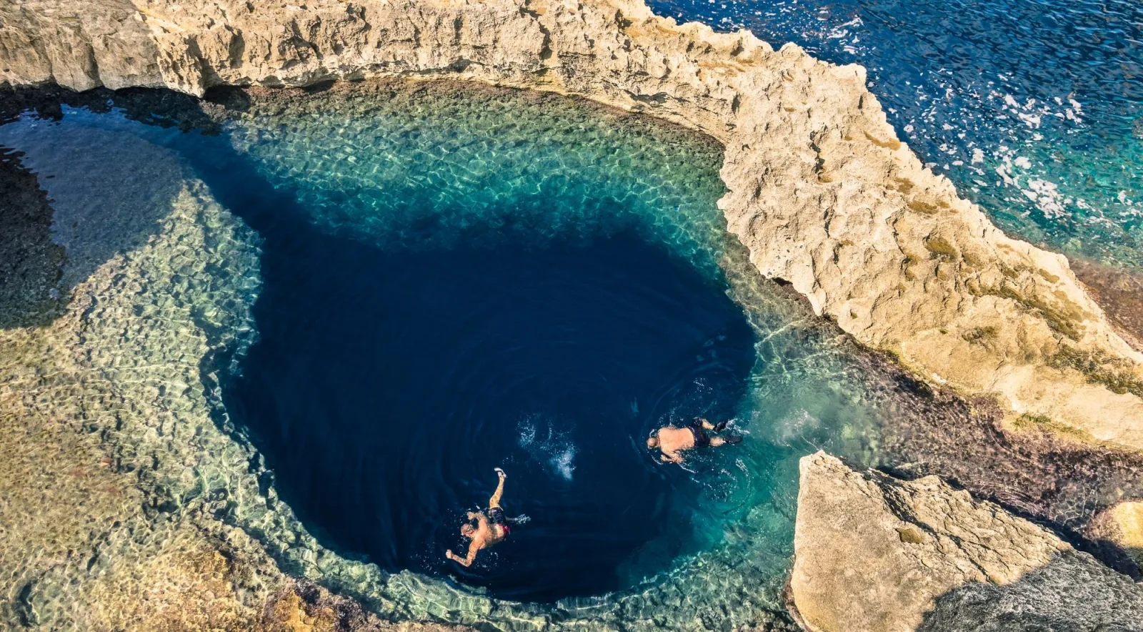 Two snorkellers in the deep circular Blue Hole rock pool at Dwejra on Gozo