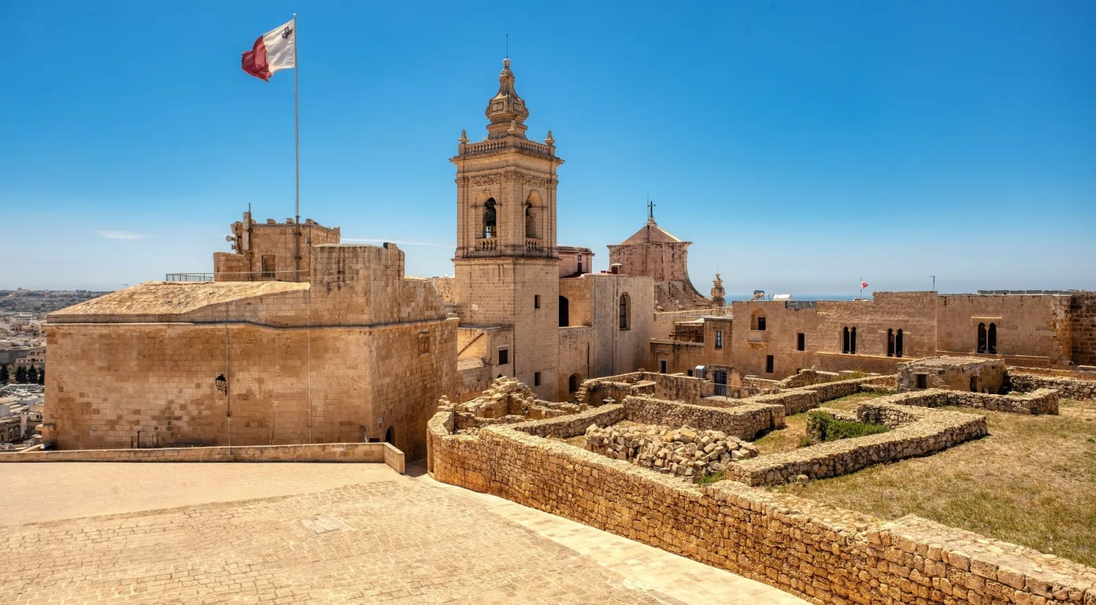The Maltese flag flying over the Citadel in Victoria with the cathedral belfry behind