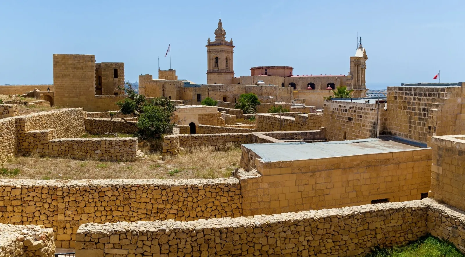 Ruined stone lanes and cleared foundations inside the Gozo Citadel with the cathedral belfry beyond