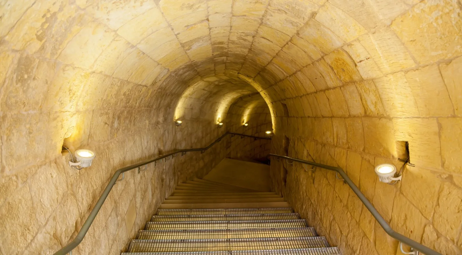 Lit vaulted limestone stairway descending inside the Gozo Citadel