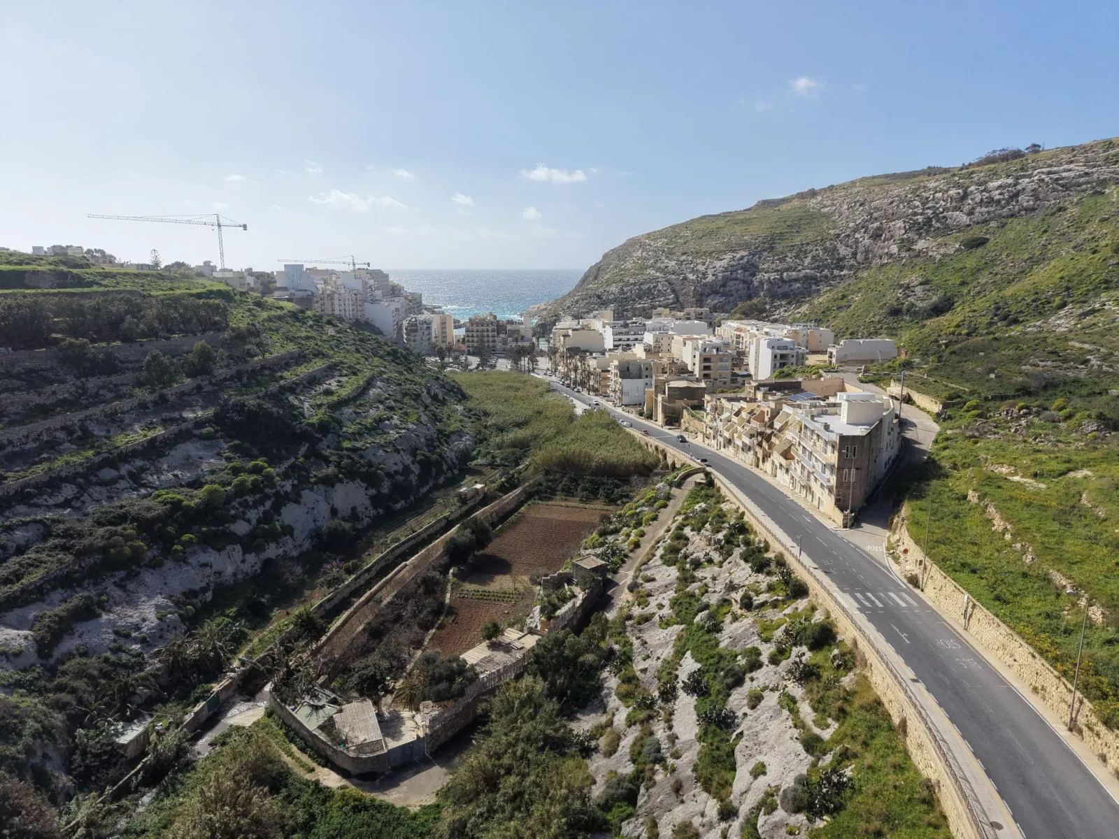 Aerial view of a road winding down to a bay on Gozo's coast