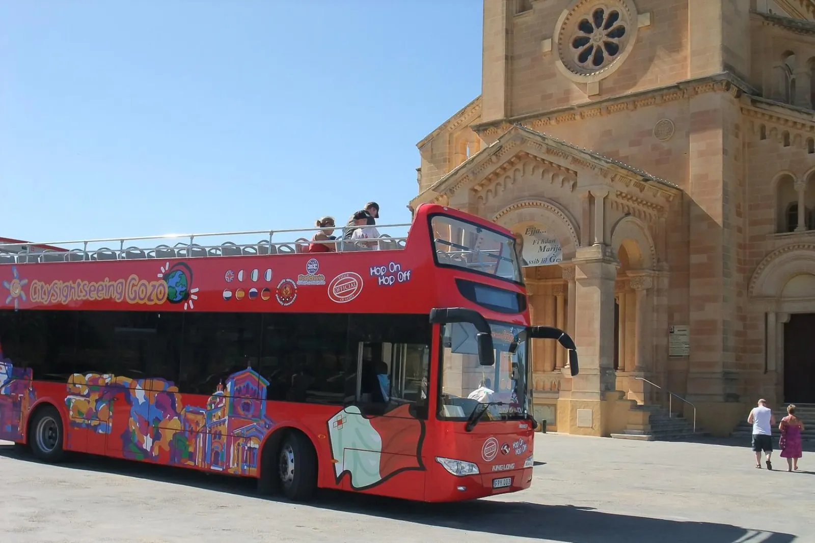 Red open-top sightseeing bus parked outside a church on Gozo