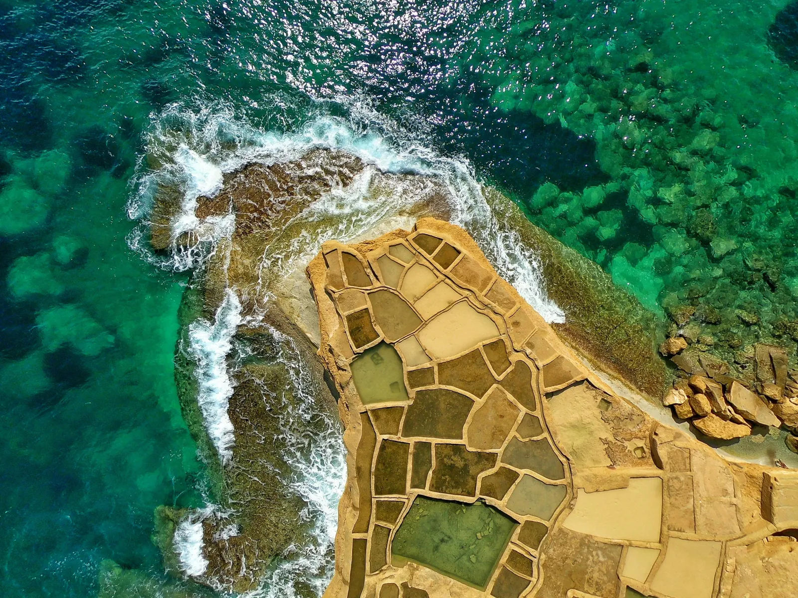 Aerial view of the Xwejni salt pans cut into Gozo's north coast beside turquoise water