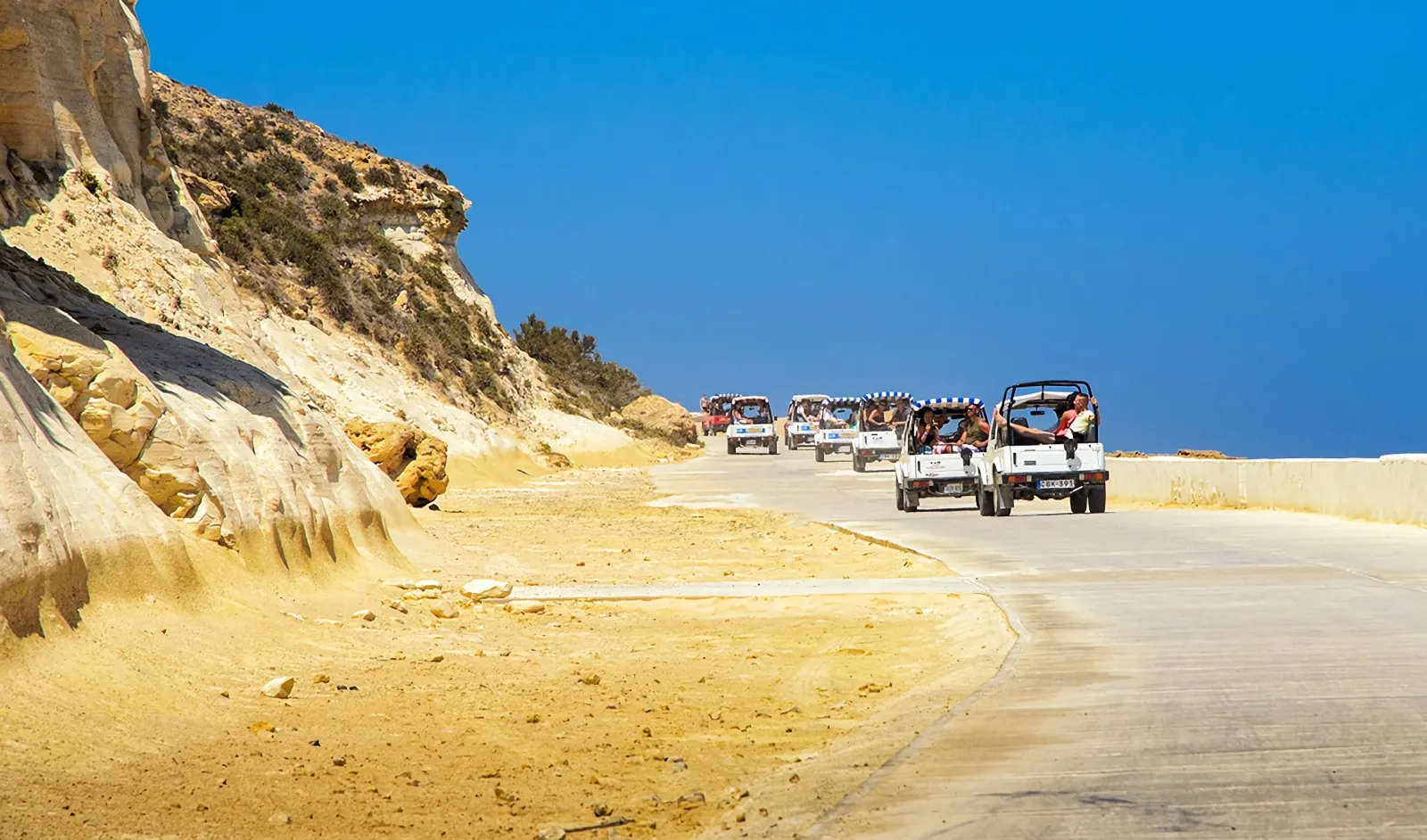 Convoy of open tour jeeps on a sandy coastal road on a Gozo jeep tour