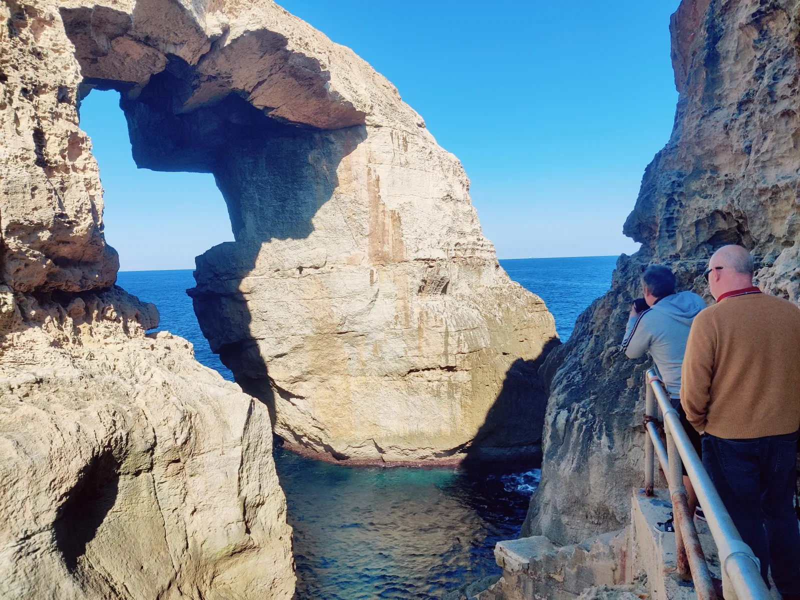 Visitors at the railing above the Wied il-Mielaħ window on Gozo's north coast